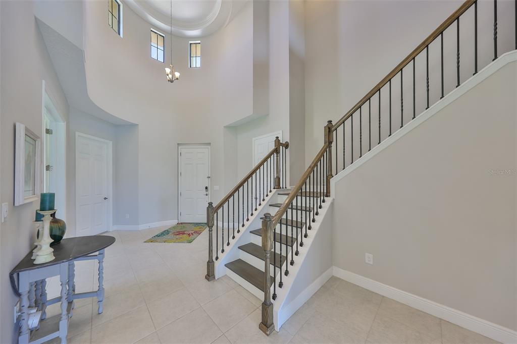 A bright foyer features a high ceiling, tile flooring, and a staircase with wooden railings — 11909 CLIMBING FERN AVENUE, RIVERVIEW, FL