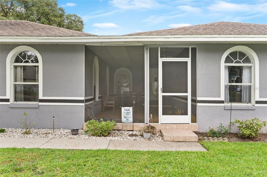 A gray house exterior features a screened-in porch, arched windows, and a concrete walkway — 2010 DEERBROOK DRIVE, LAKELAND, FL
