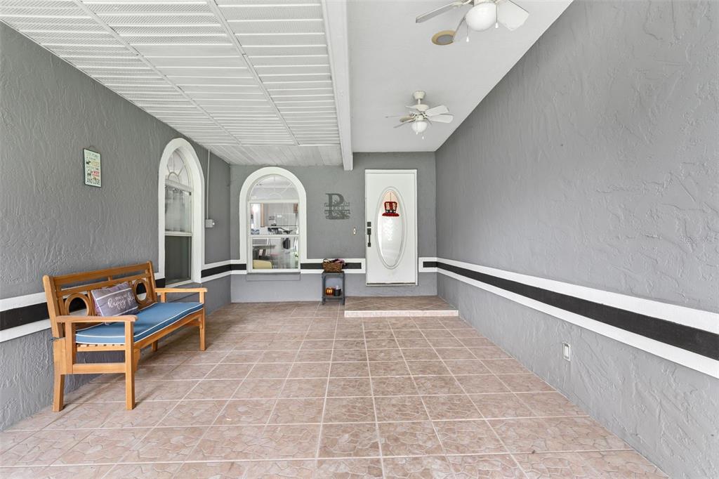 A covered porch features gray stucco walls, tiled flooring, a wooden bench, and two ceiling fans — 2010 DEERBROOK DRIVE, LAKELAND, FL