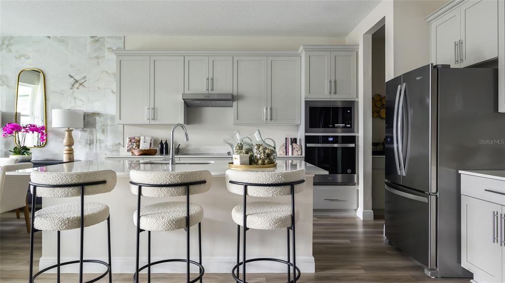 A modern kitchen features light gray cabinets, a white island with bar stools, and stainless appliances — 33572 HAMMOCK BEACH WAY, DADE CITY, FL
