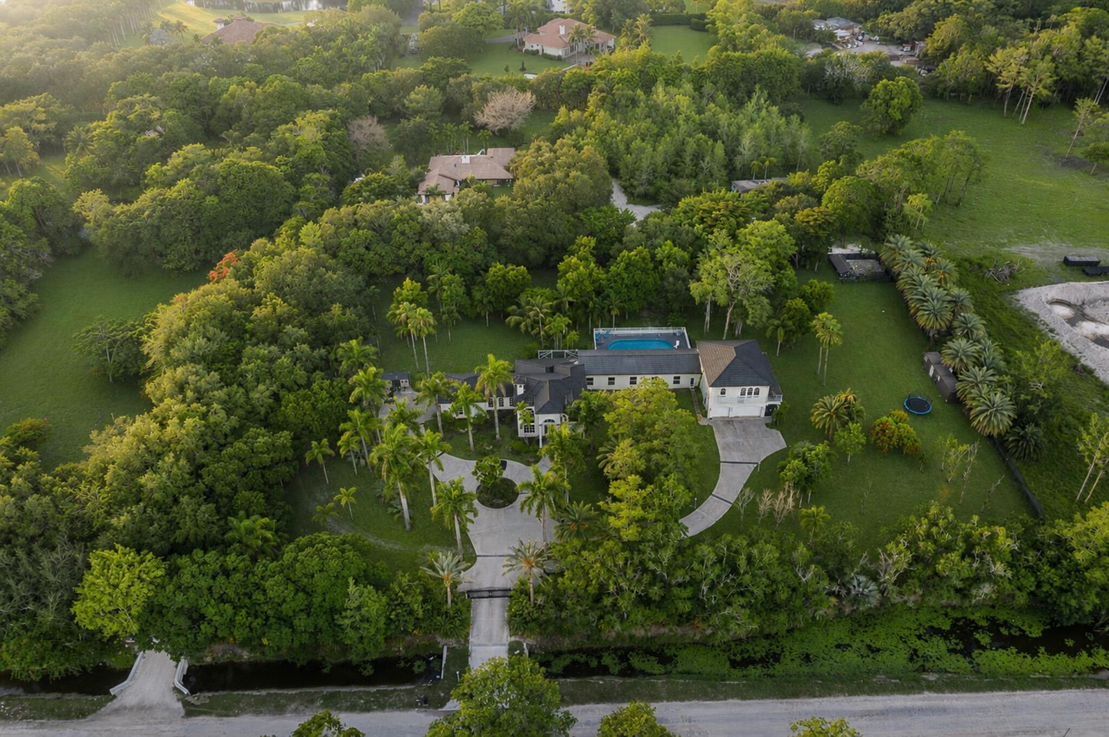 An aerial view shows a large house with a pool surrounded by lush green trees — 6911 NW 84th Avenue, Parkland FL 33067, PARKLAND, FL