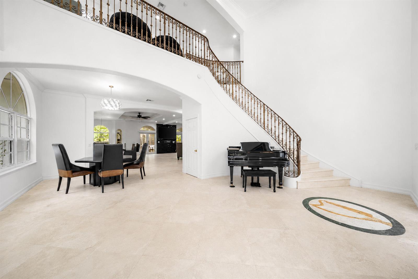 A grand foyer features a curved staircase, a black grand piano, and light tile flooring — 6911 NW 84th Avenue, Parkland FL 33067, PARKLAND, FL