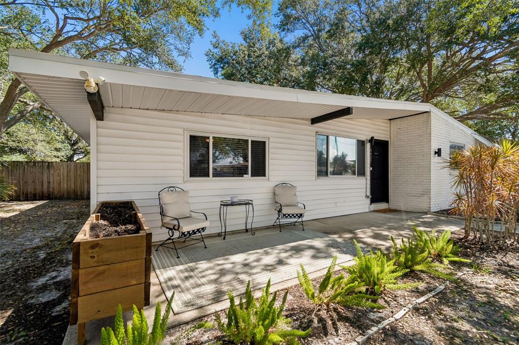 A white house exterior features a covered patio with two chairs and a wooden planter — 4437 W BAY AVENUE, TAMPA, FL