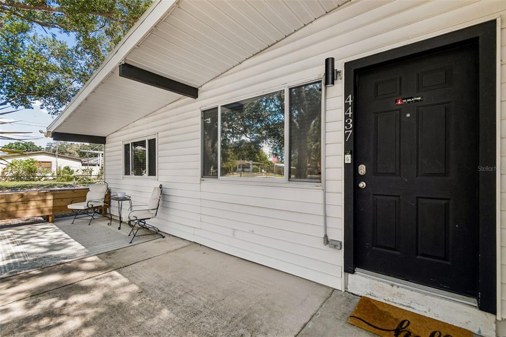A white-sided house exterior features a black front door, a large window, and a patio — 4437 W BAY AVENUE, TAMPA, FL