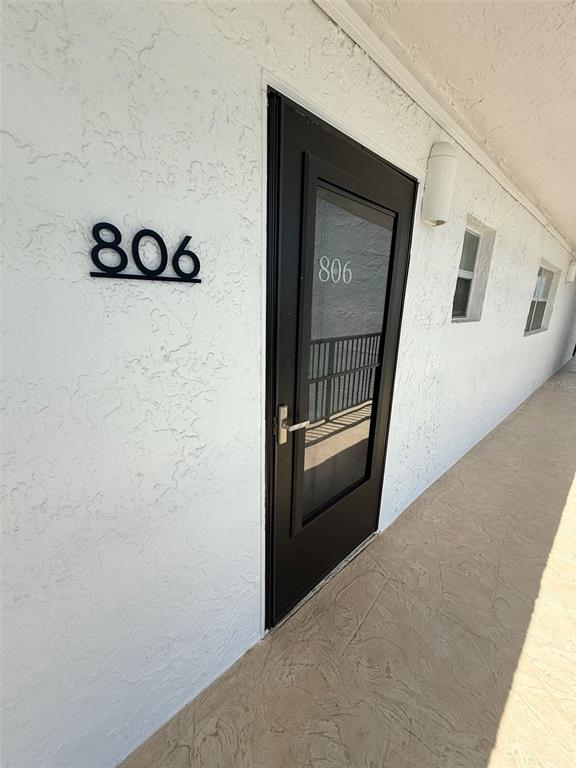A black door with the number 806 is set into a white textured exterior wall — 9393 MIDNIGHT PASS ROAD UNIT 806, SARASOTA, FL