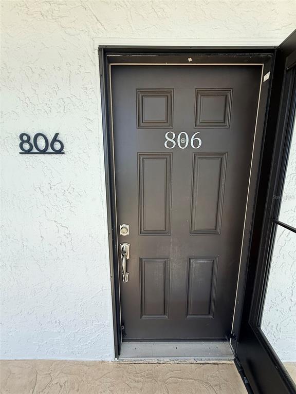 A dark brown front door with the number 806 is set into a white stucco wall — 9393 MIDNIGHT PASS ROAD UNIT 806, SARASOTA, FL