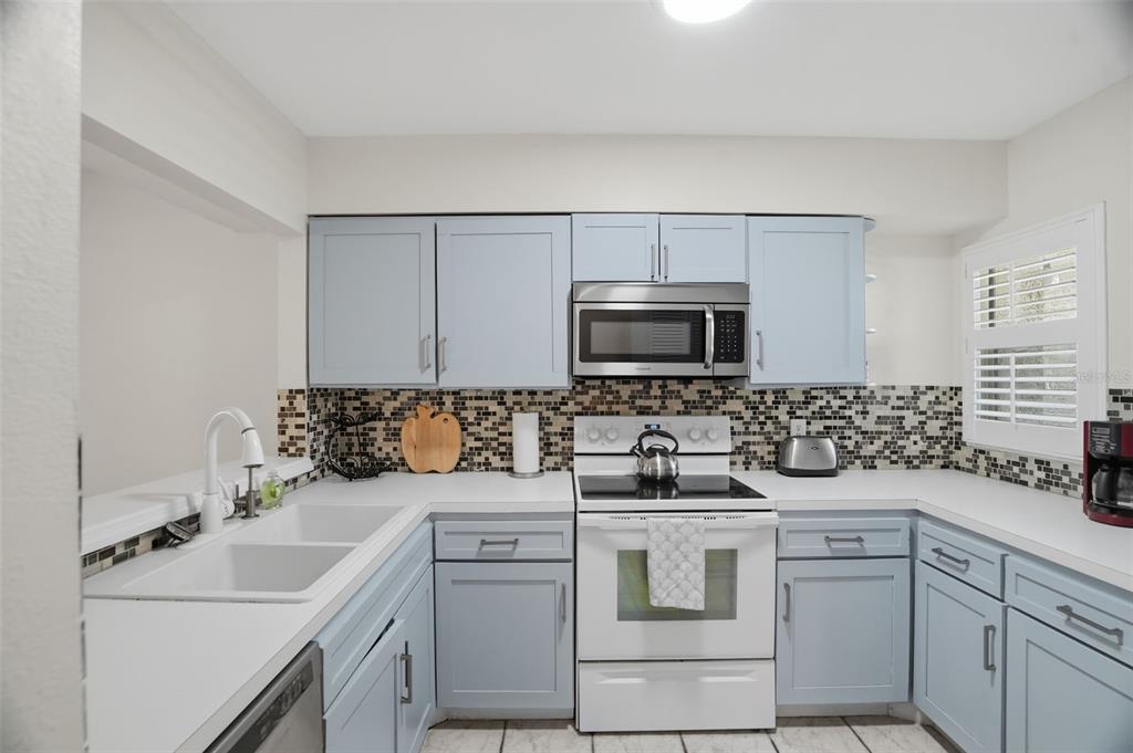 A kitchen features light blue cabinets, white countertops, a mosaic tile backsplash, and stainless appliances — 5557 SEA FOREST DRIVE UNIT 215, NEW PORT RICHEY, FL