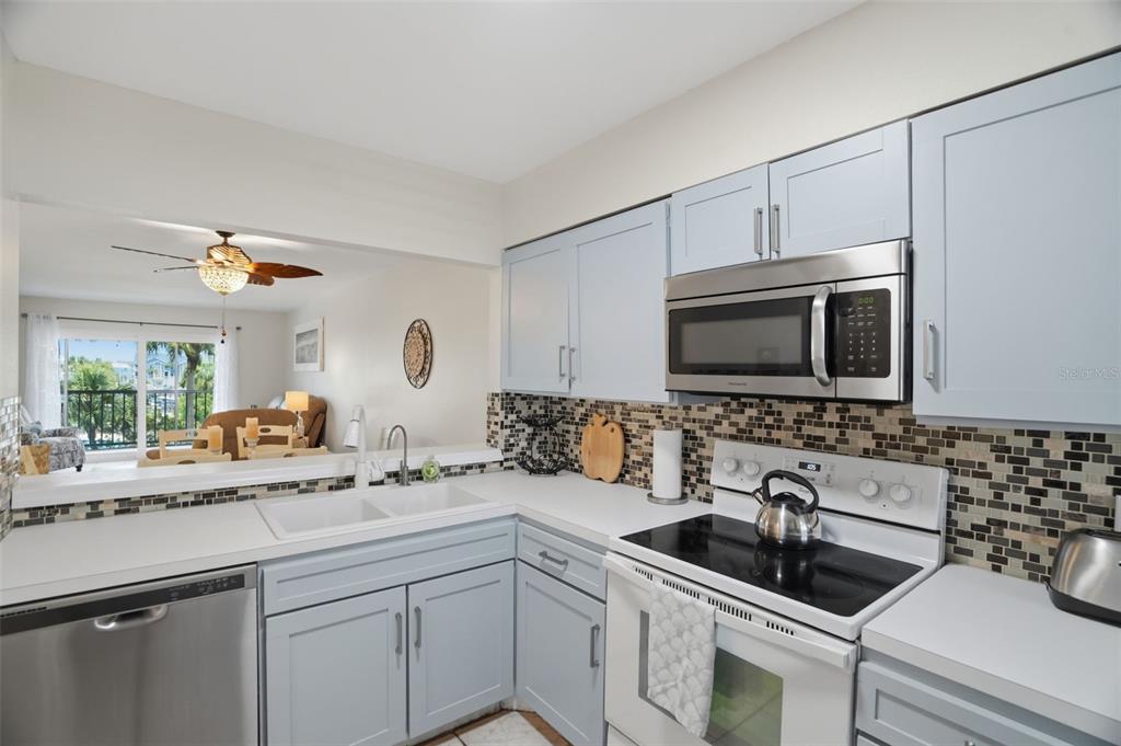 A kitchen features light blue cabinets, stainless steel appliances, and a mosaic tile backsplash — 5557 SEA FOREST DRIVE UNIT 215, NEW PORT RICHEY, FL