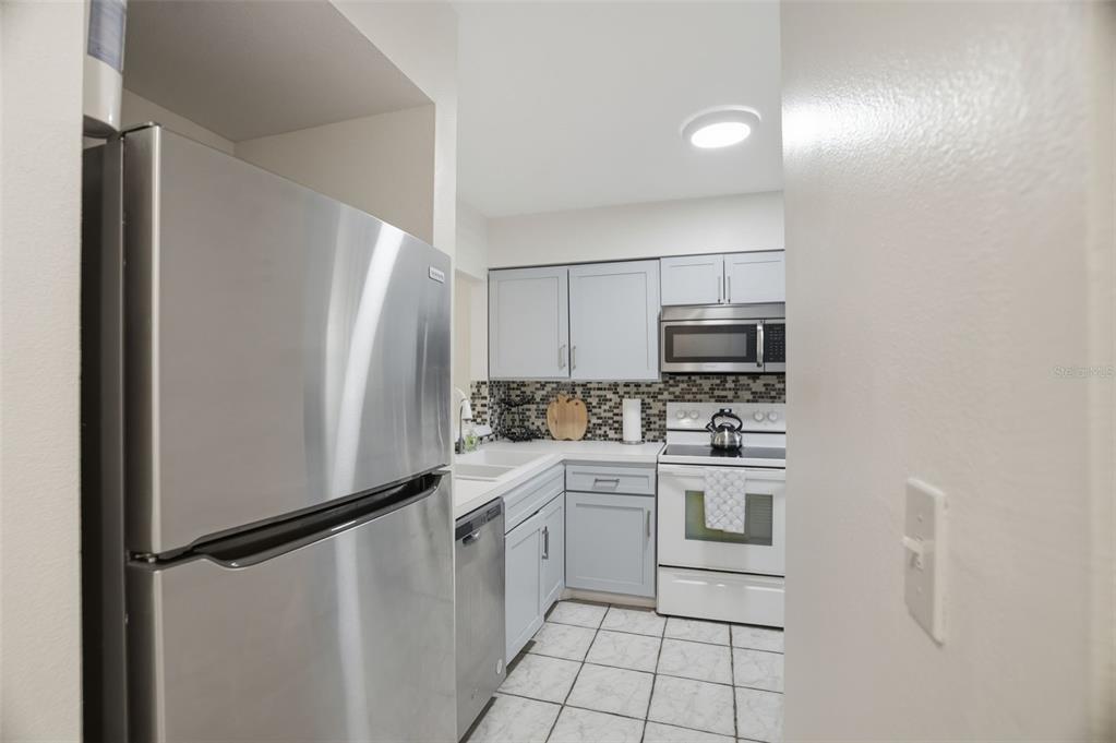 A galley kitchen features stainless steel appliances, light gray cabinets, and white tiled flooring — 5557 SEA FOREST DRIVE UNIT 215, NEW PORT RICHEY, FL