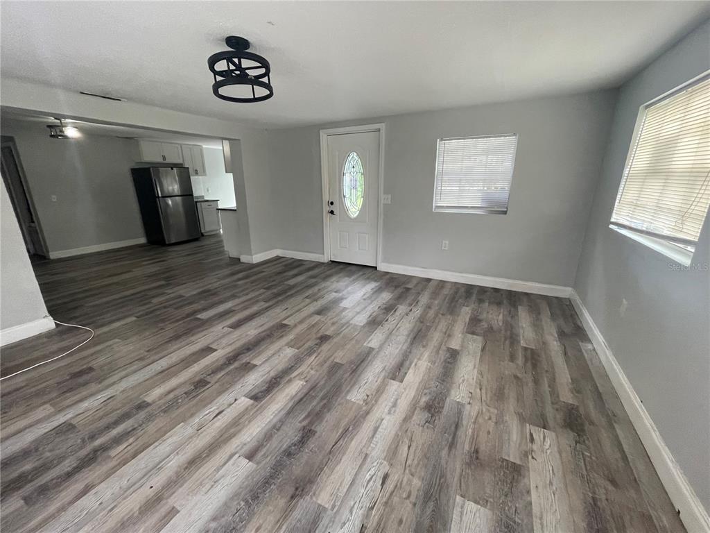 An open-concept living area features gray wood-look flooring, light gray walls, and a kitchen view — 1225 NEMETH STREET, AUBURNDALE, FL