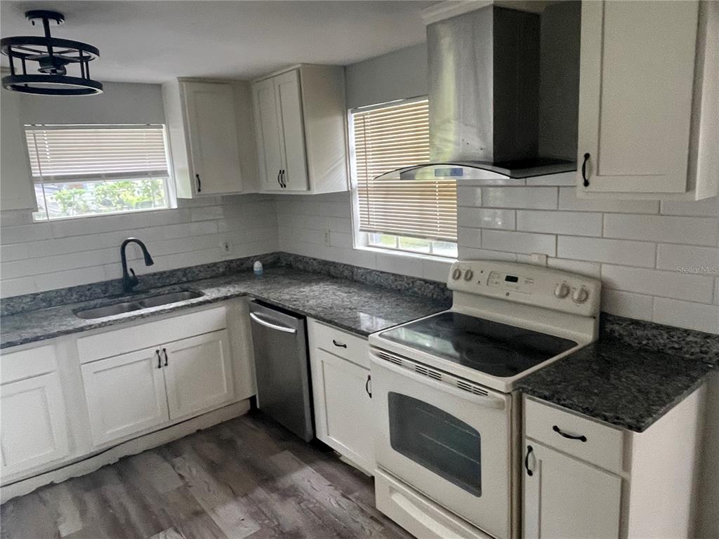 A kitchen features white cabinets, granite countertops, a stainless steel range hood, and subway tile — 1225 NEMETH STREET, AUBURNDALE, FL