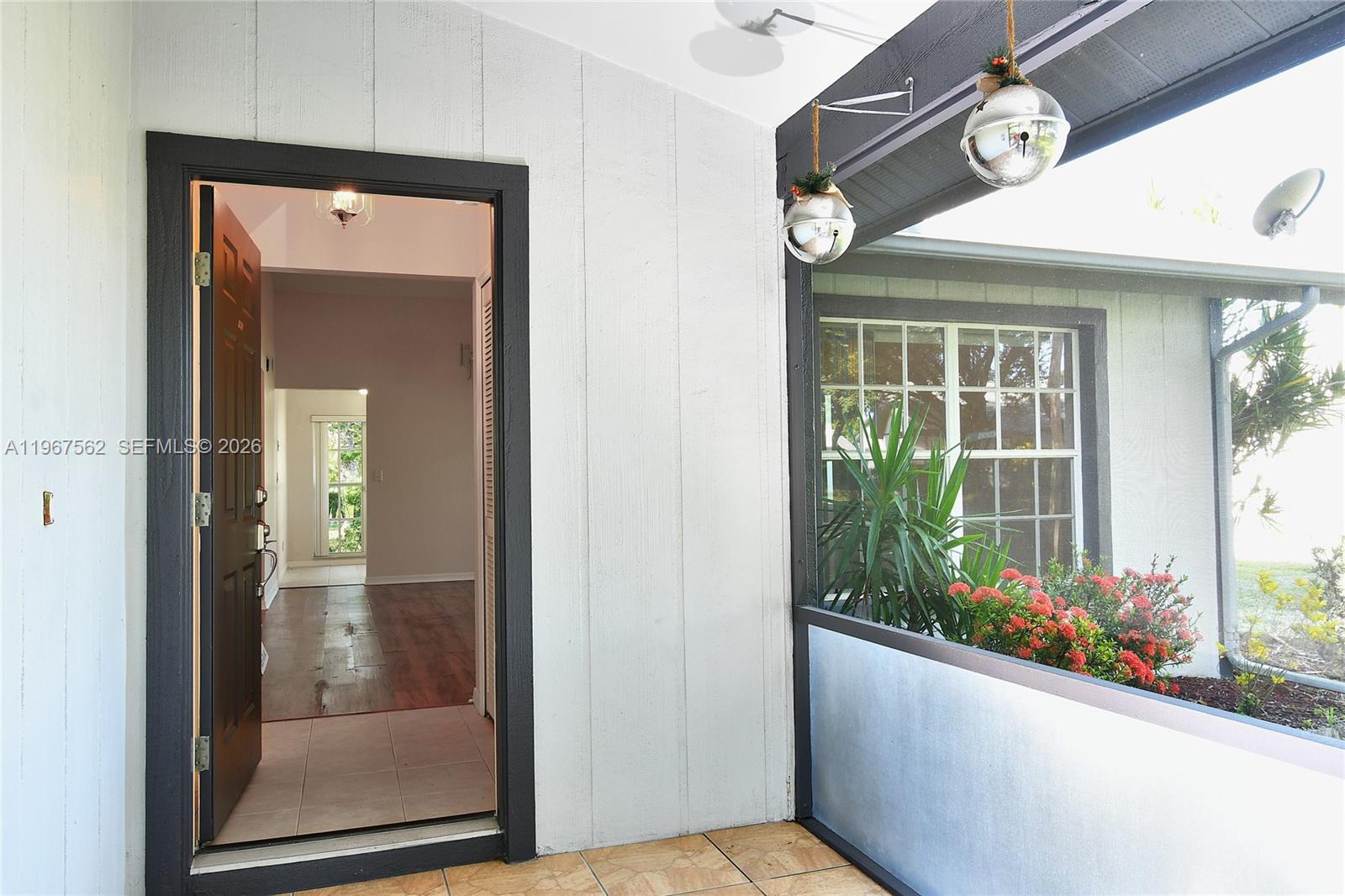 An open front door reveals an interior entryway with tile flooring and wood-look flooring beyond — 10655 Vanceboro Ct., Lehigh Acres FL 33936, LEHIGH ACRES, FL