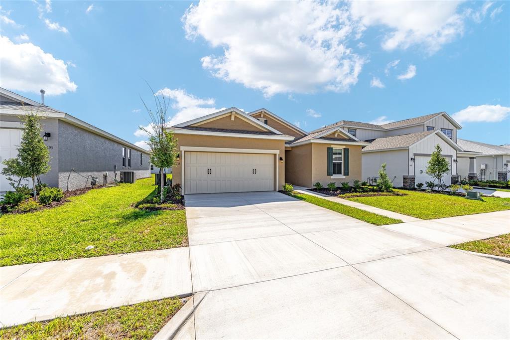 A tan single-story house with a two-car garage and a concrete driveway under a blue sky — 5705 SW 71ST AVENUE, OCALA, FL