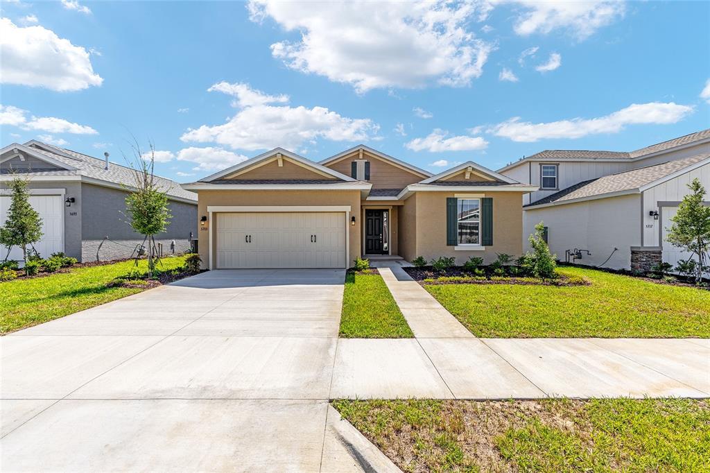 A tan single-story house features a two-car garage, a front walkway, and a landscaped lawn — 5705 SW 71ST AVENUE, OCALA, FL