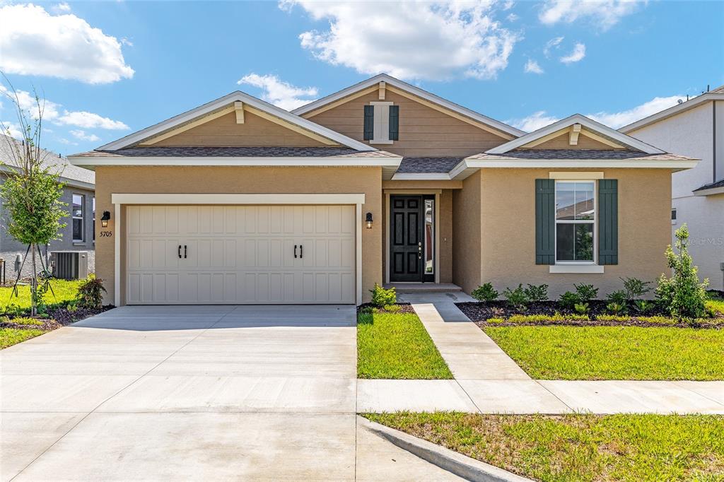 A single-story suburban house with a tan stucco exterior, two gables, and a concrete driveway — 5705 SW 71ST AVENUE, OCALA, FL