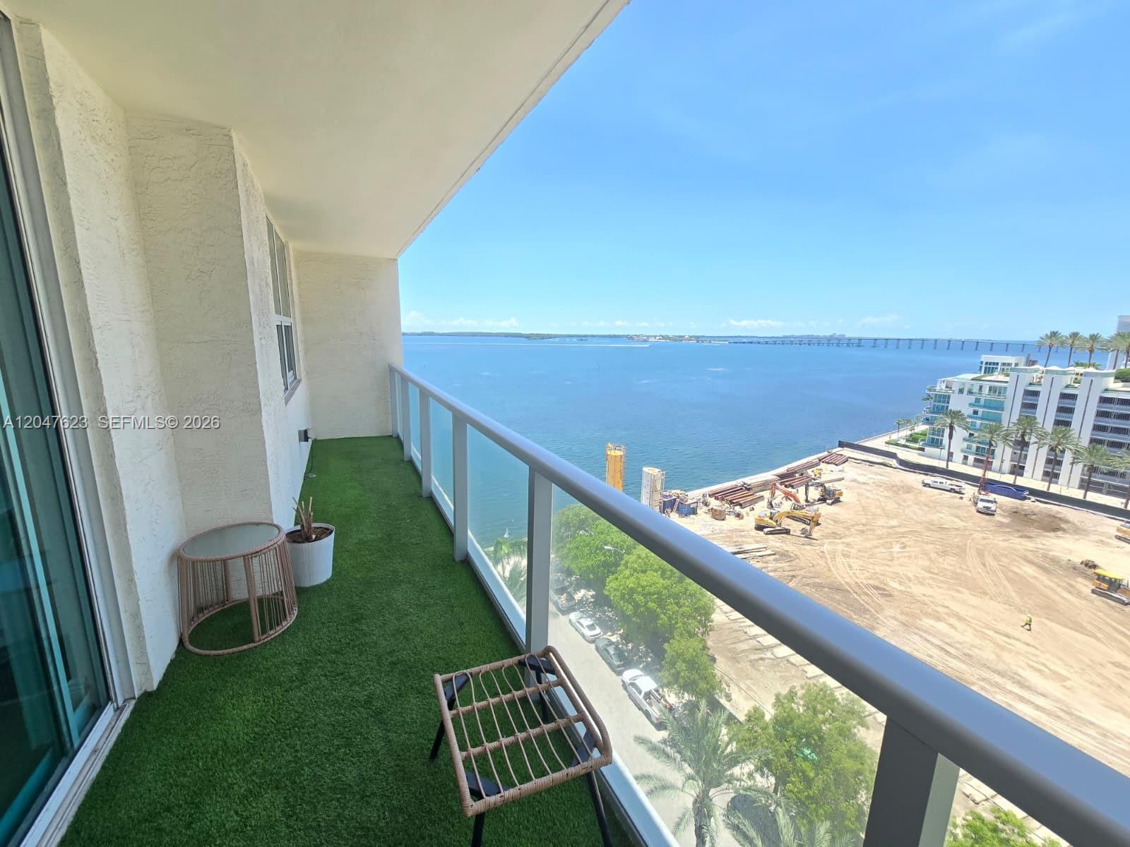 A balcony with artificial turf flooring overlooks a construction site and the ocean — MIAMI, FL