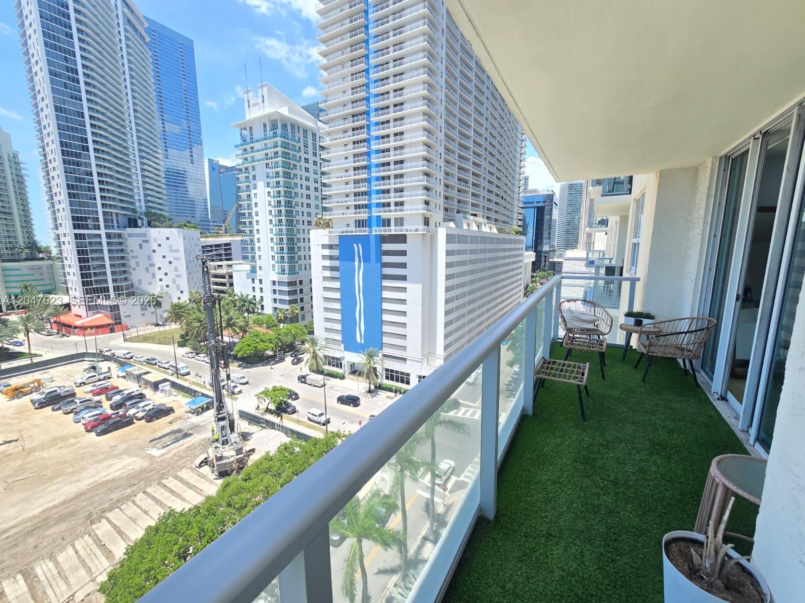 A balcony with artificial turf, patio furniture, and a view of city skyscrapers and construction — MIAMI, FL