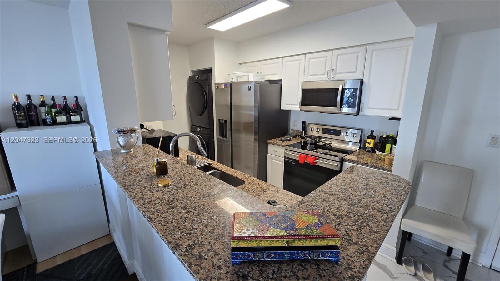 A kitchen features granite countertops, white cabinetry, stainless steel appliances, and a stacked laundry unit — MIAMI, FL