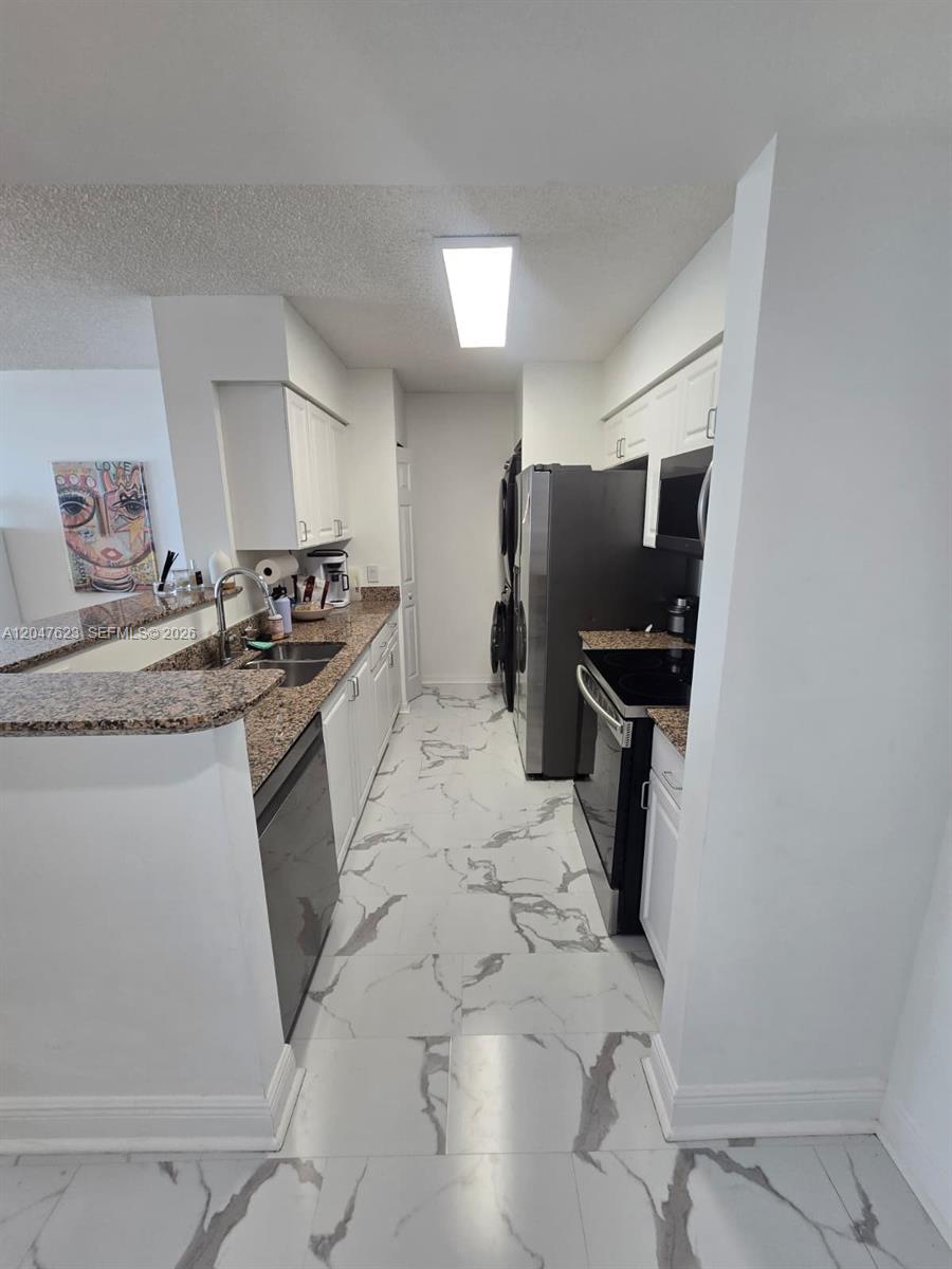 A galley kitchen features white cabinets, granite countertops, stainless steel appliances, and marble-look tile flooring — MIAMI, FL