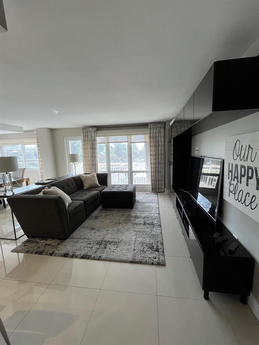 A modern living room features a dark gray sectional sofa, a patterned rug, and a television — 133 N Pompano Beach Boulevard # 211, Pompano Beach FL 33062, POMPANO BEACH, FL