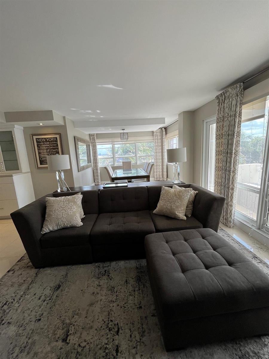 A living room with a dark gray sectional sofa, ottoman, and an adjacent dining area — 133 N Pompano Beach Boulevard # 211, Pompano Beach FL 33062, POMPANO BEACH, FL