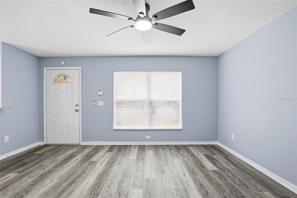 An empty room with light blue walls, wood-look flooring, a ceiling fan, and a door — 8309 N 12TH STREET, TAMPA, FL
