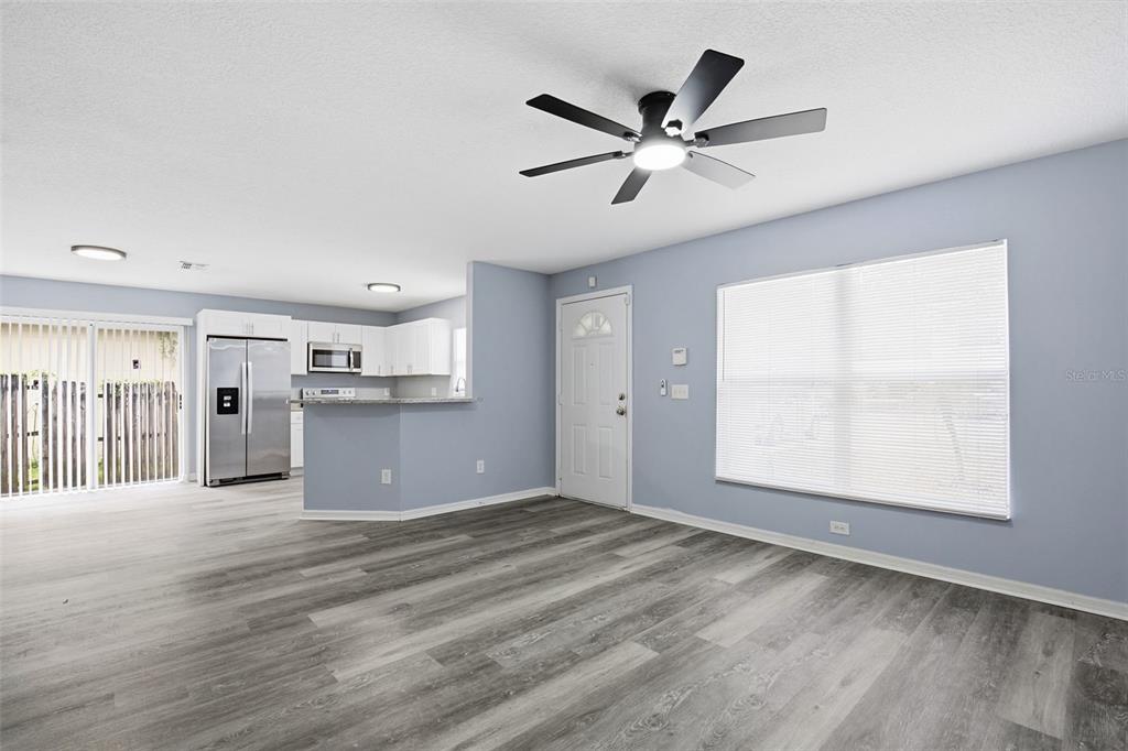 An open-concept living room with light blue walls, wood-look flooring, and an adjacent kitchen — 8309 N 12TH STREET, TAMPA, FL