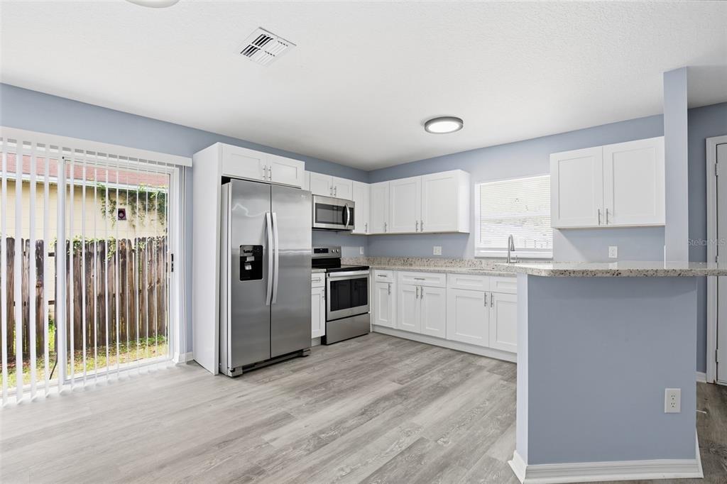 A kitchen with white cabinets, stainless steel appliances, granite countertops, and light wood-look flooring — 8309 N 12TH STREET, TAMPA, FL