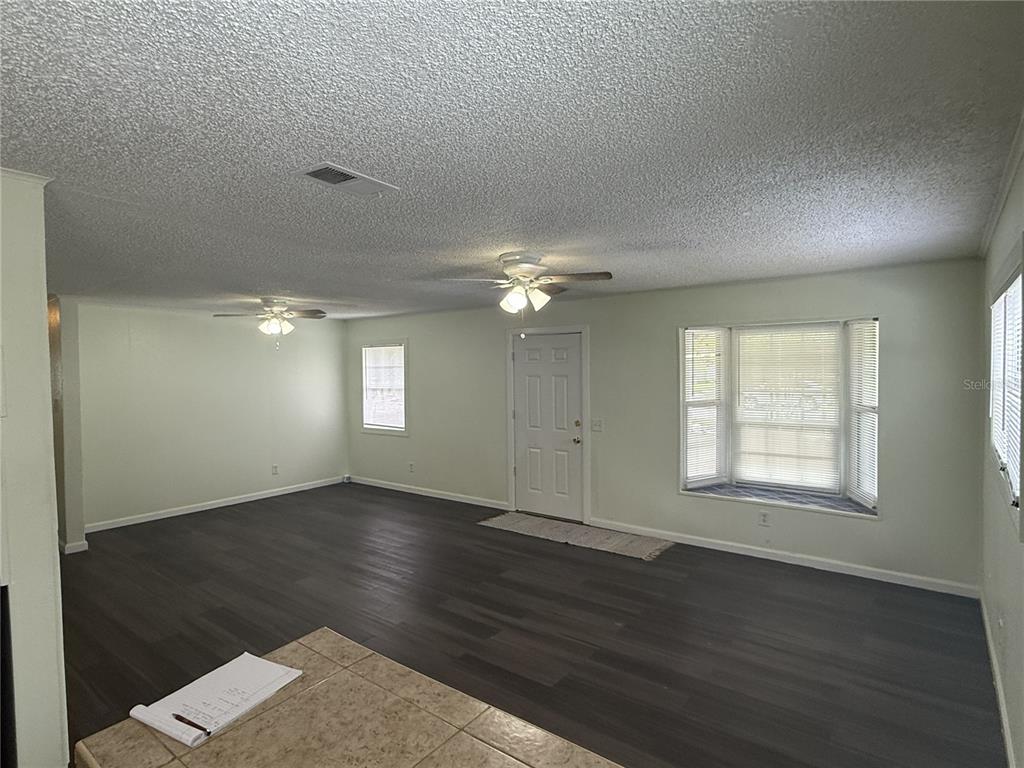An empty living room features dark wood-look flooring, light-colored walls, two ceiling fans, and windows — 102 GROVE STREET, ORLANDO, FL