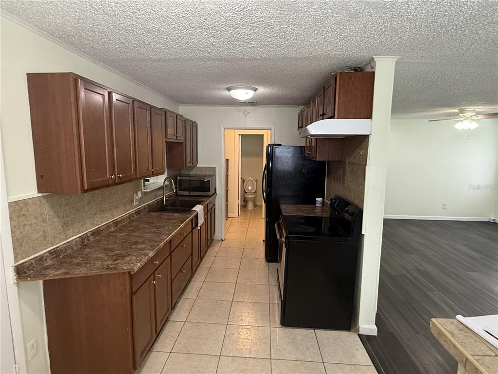 A kitchen with brown cabinets, dark countertops, black appliances, and tile flooring — 102 GROVE STREET, ORLANDO, FL