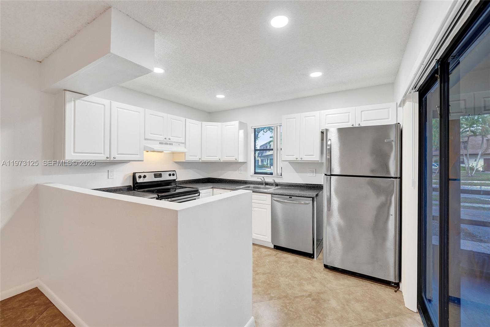 A kitchen features white cabinets, stainless steel appliances, dark countertops, and tile flooring — 9340 SW 61st Way # B, Boca Raton FL 33428, BOCA RATON, FL