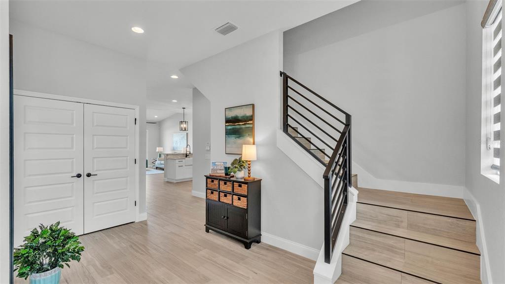 An entryway features light wood-look flooring, a staircase with black railings, and double closet doors — 1178 WINDJAMMER DRIVE, LAKELAND, FL