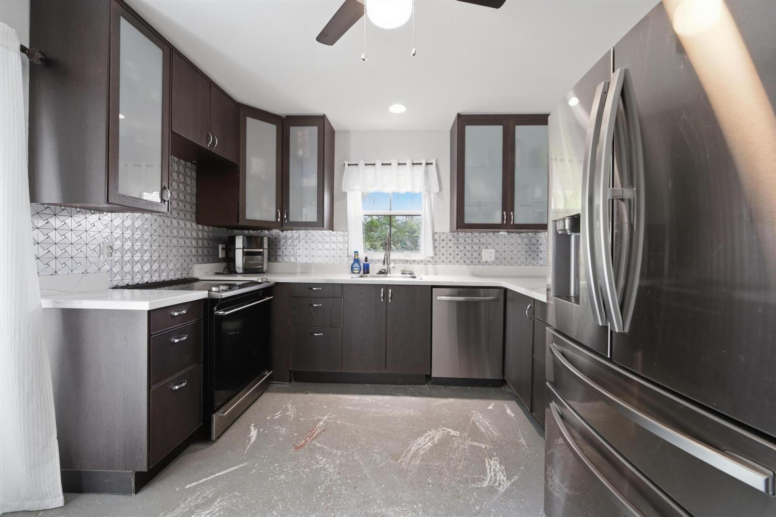 A kitchen features dark wood cabinets, stainless steel appliances, a patterned backsplash, and unfinished flooring — 8417 NW 40th Court, Sunrise FL 33351, SUNRISE, FL