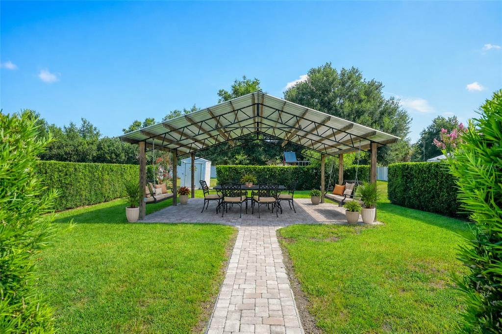 A backyard features a covered patio with a dining set and two hanging porch swings — 39036 ROSE STREET, UMATILLA, FL