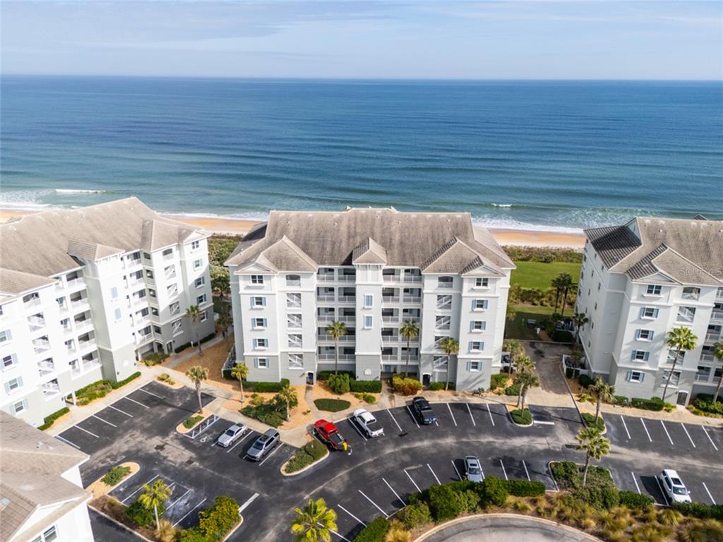 An aerial view shows three multi-story apartment buildings situated along a sandy beach and ocean — 600 CINNAMON BEACH WAY UNIT 521, PALM COAST, FL