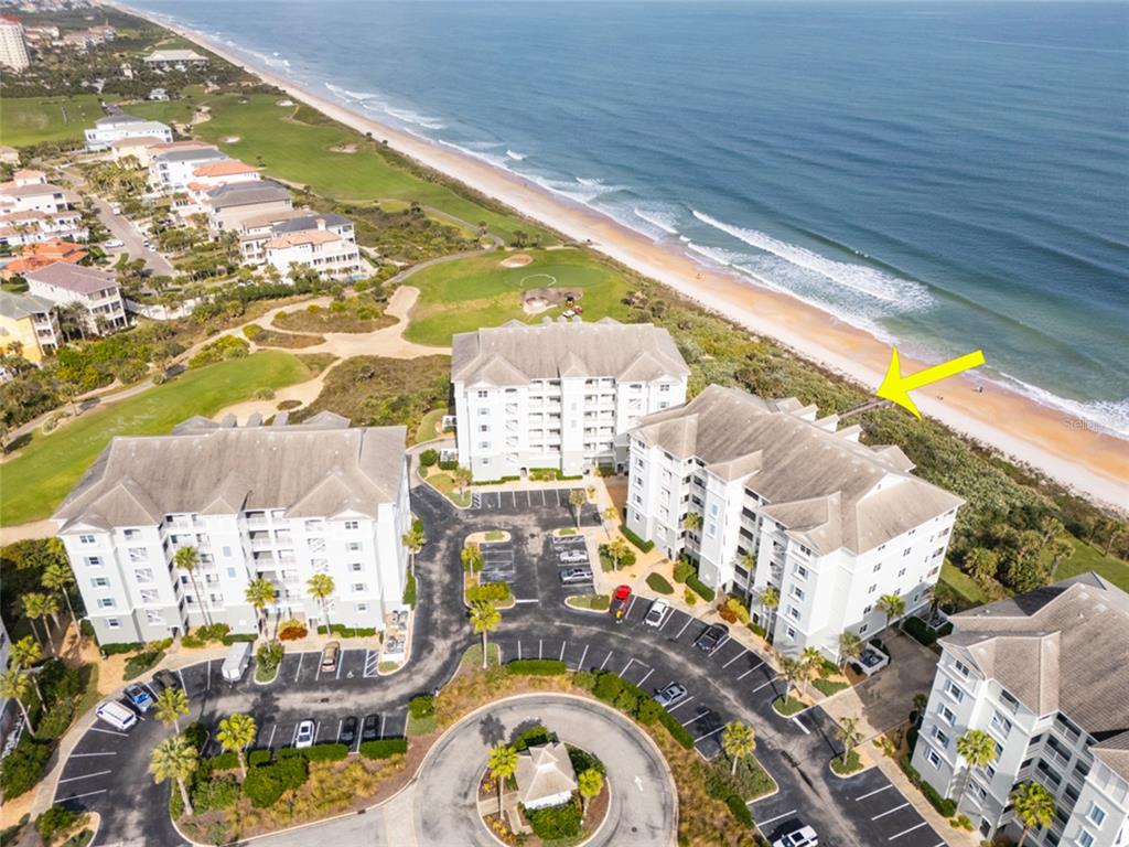 An aerial view shows multi-story residential buildings near a beach with a wooden walkway — 600 CINNAMON BEACH WAY UNIT 521, PALM COAST, FL