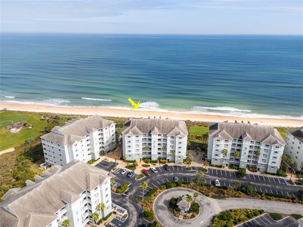 An aerial view shows several multi-story beachfront condominium buildings with parking lots and the ocean — 600 CINNAMON BEACH WAY UNIT 521, PALM COAST, FL
