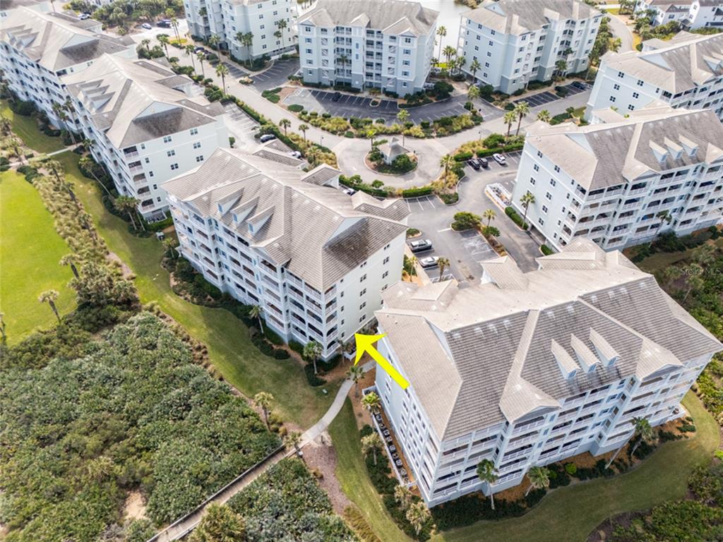 An aerial view shows several multi-story apartment buildings with a yellow arrow pointing toward one — 600 CINNAMON BEACH WAY UNIT 521, PALM COAST, FL