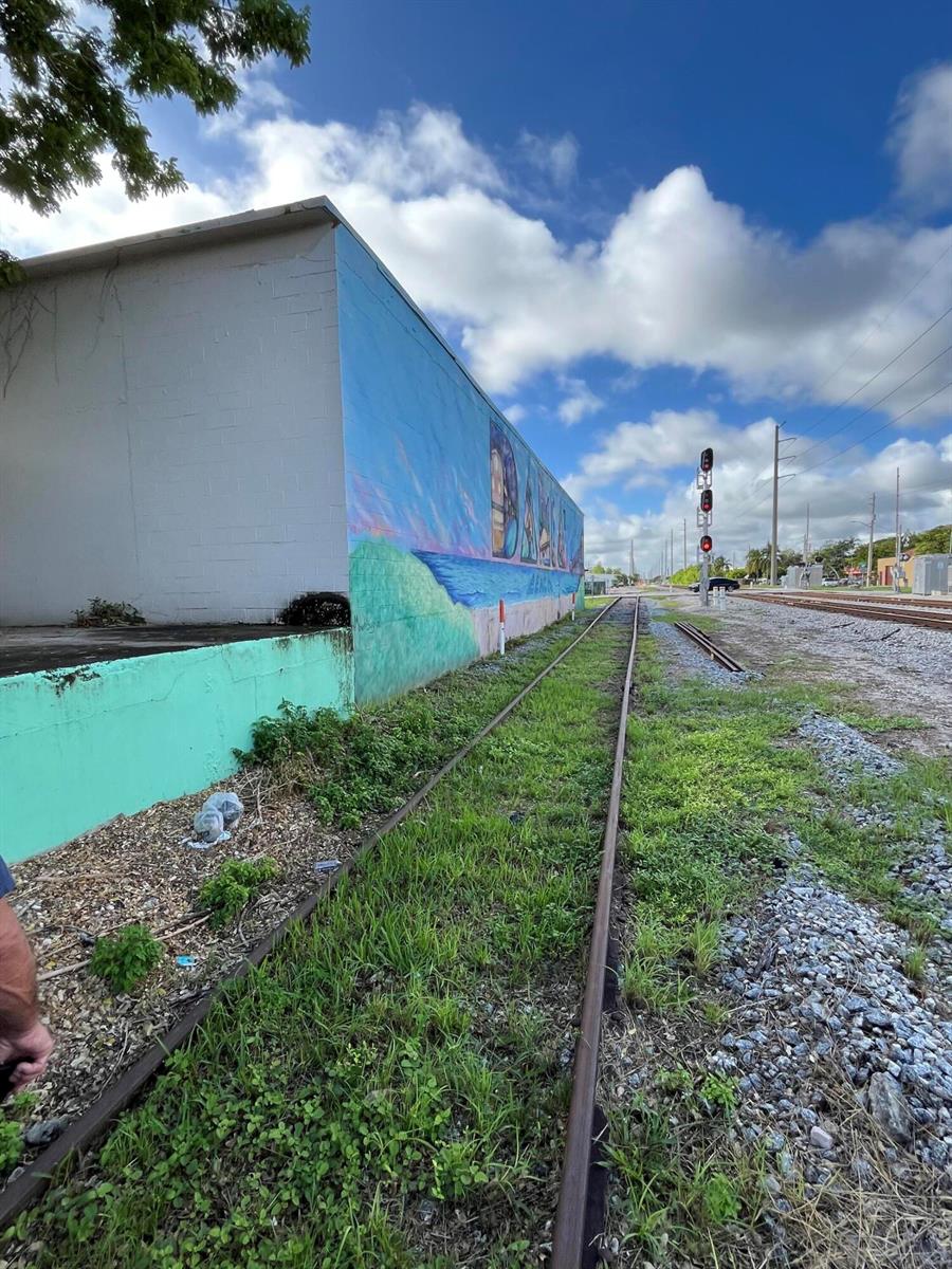 A mural-painted building stands beside a set of railroad tracks under a cloudy blue sky — 5 NW 3rd Avenue, Dania Beach FL 33004, DANIA BEACH, FL