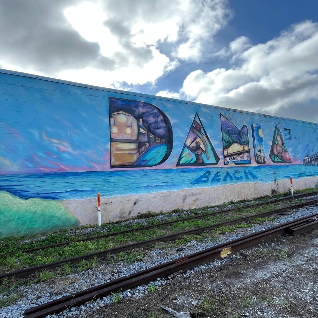 A large mural spelling "DANIA BEACH" is painted on a wall beside railroad tracks — 5 NW 3rd Avenue, Dania Beach FL 33004, DANIA BEACH, FL