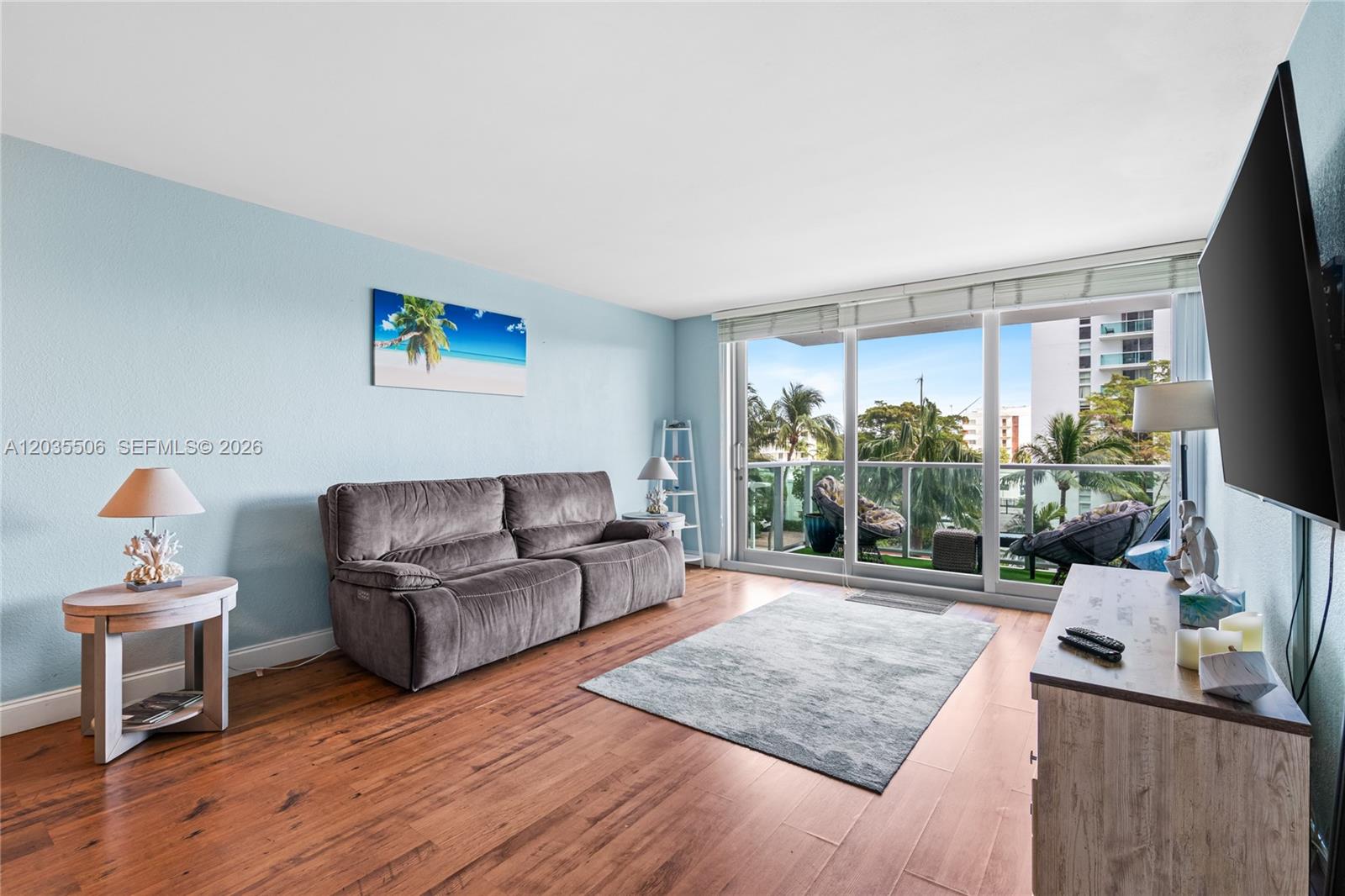 A living room features a gray sofa, wood flooring, and a balcony with palm trees — 1000 West Ave # 308, Miami Beach FL 33139, MIAMI BEACH, FL