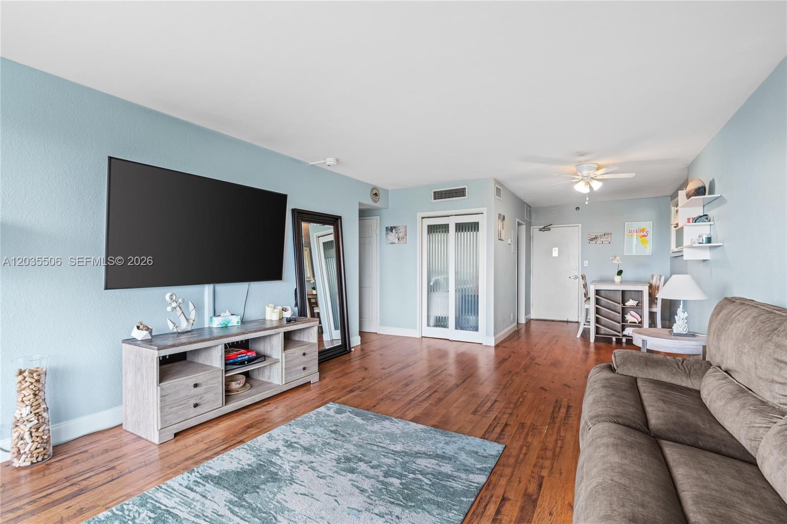A living room features light blue walls, wood flooring, a large television, and a sofa — 1000 West Ave # 308, Miami Beach FL 33139, MIAMI BEACH, FL