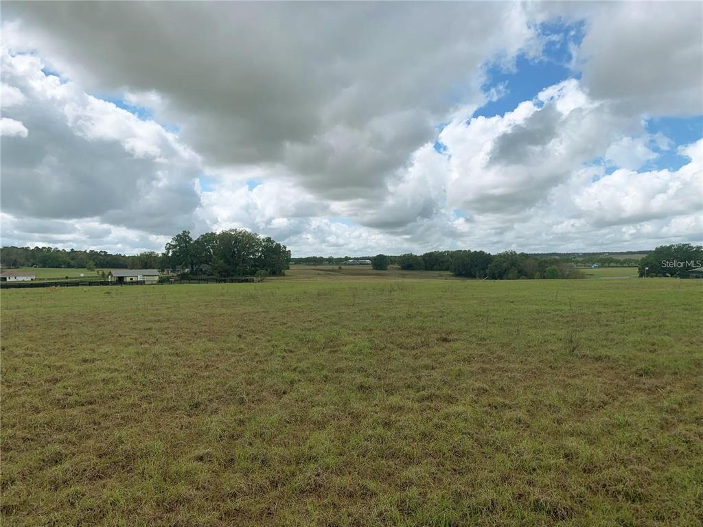 A wide, grassy field under a cloudy sky with a small building in the distance — 21635 SW 10TH STREET, DUNNELLON, FL