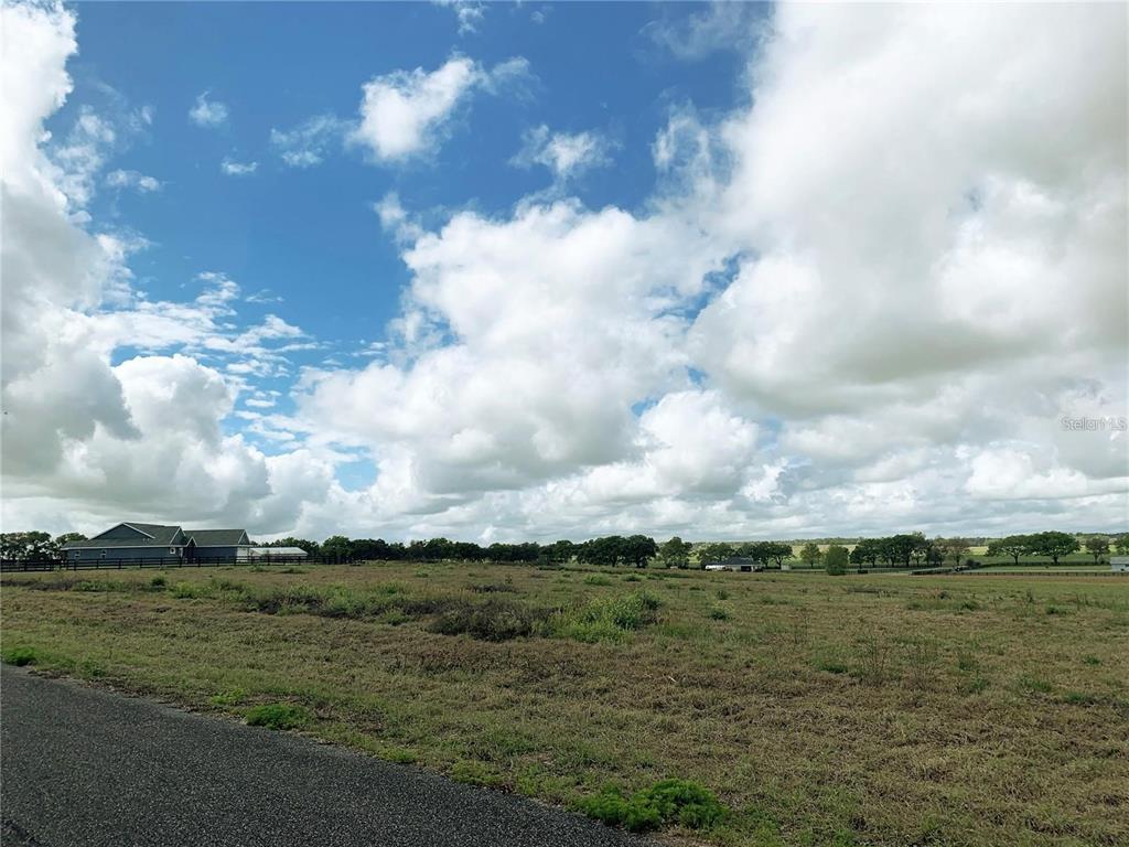 A wide, grassy field under a cloudy blue sky with a house in the distance — 21635 SW 10TH STREET, DUNNELLON, FL