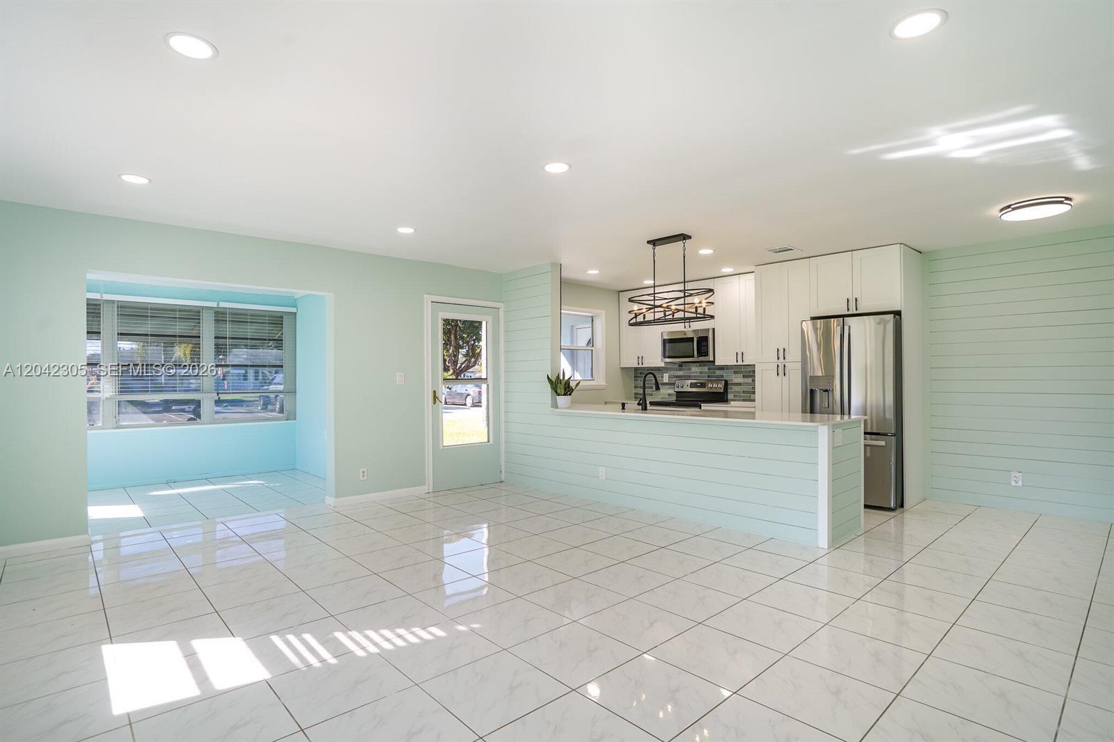 A kitchen with white cabinets and a light green shiplap island overlooks a tiled room — 560 High Point Dr # D, Delray Beach FL 33445, DELRAY BEACH, FL