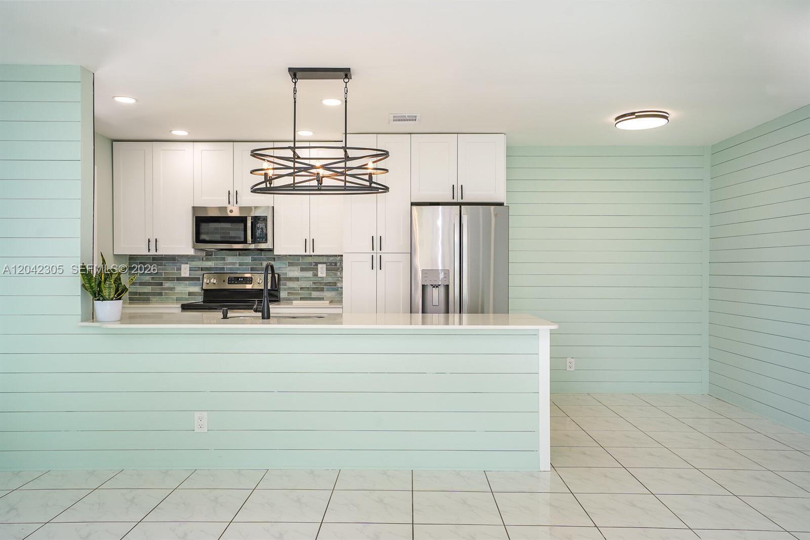 A kitchen features white cabinets, a light green shiplap island, and a modern chandelier — 560 High Point Dr # D, Delray Beach FL 33445, DELRAY BEACH, FL