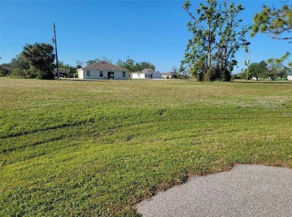 A grassy, vacant lot sits in front of a residential house under a clear sky — 25172 CADIZ DRIVE, PUNTA GORDA, FL