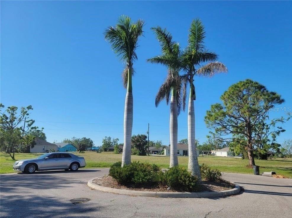 A silver sedan is parked near a circular island featuring three tall palm trees — 25172 CADIZ DRIVE, PUNTA GORDA, FL