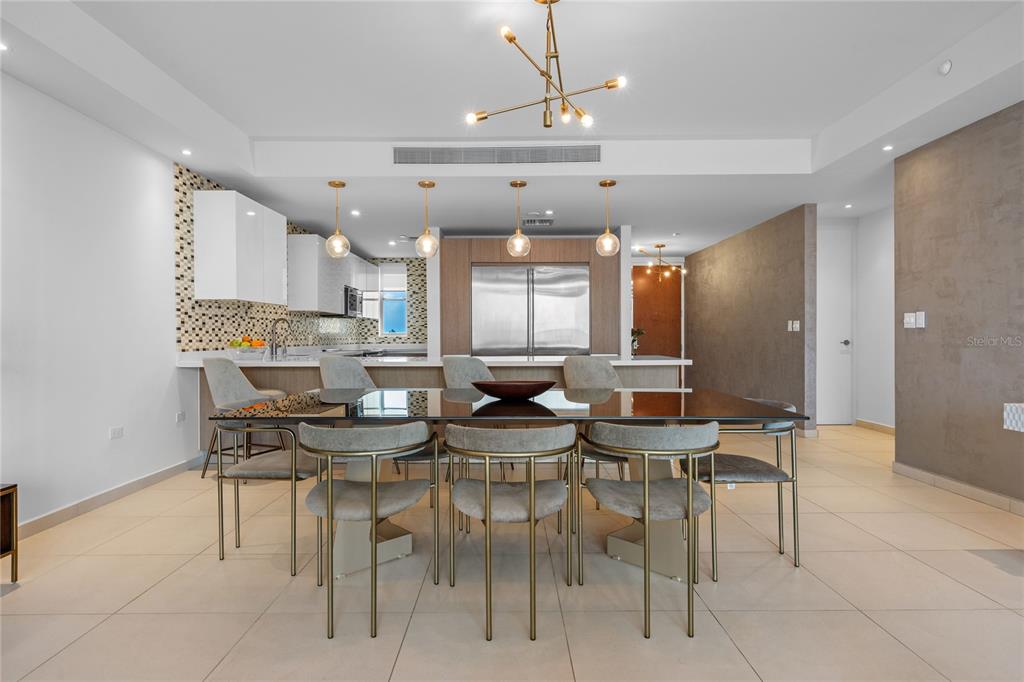 A modern dining area features a glass-topped table, upholstered chairs, and an open-concept kitchen — 25 MUNOZ RIVERA UNIT 902, SAN JUAN, PR