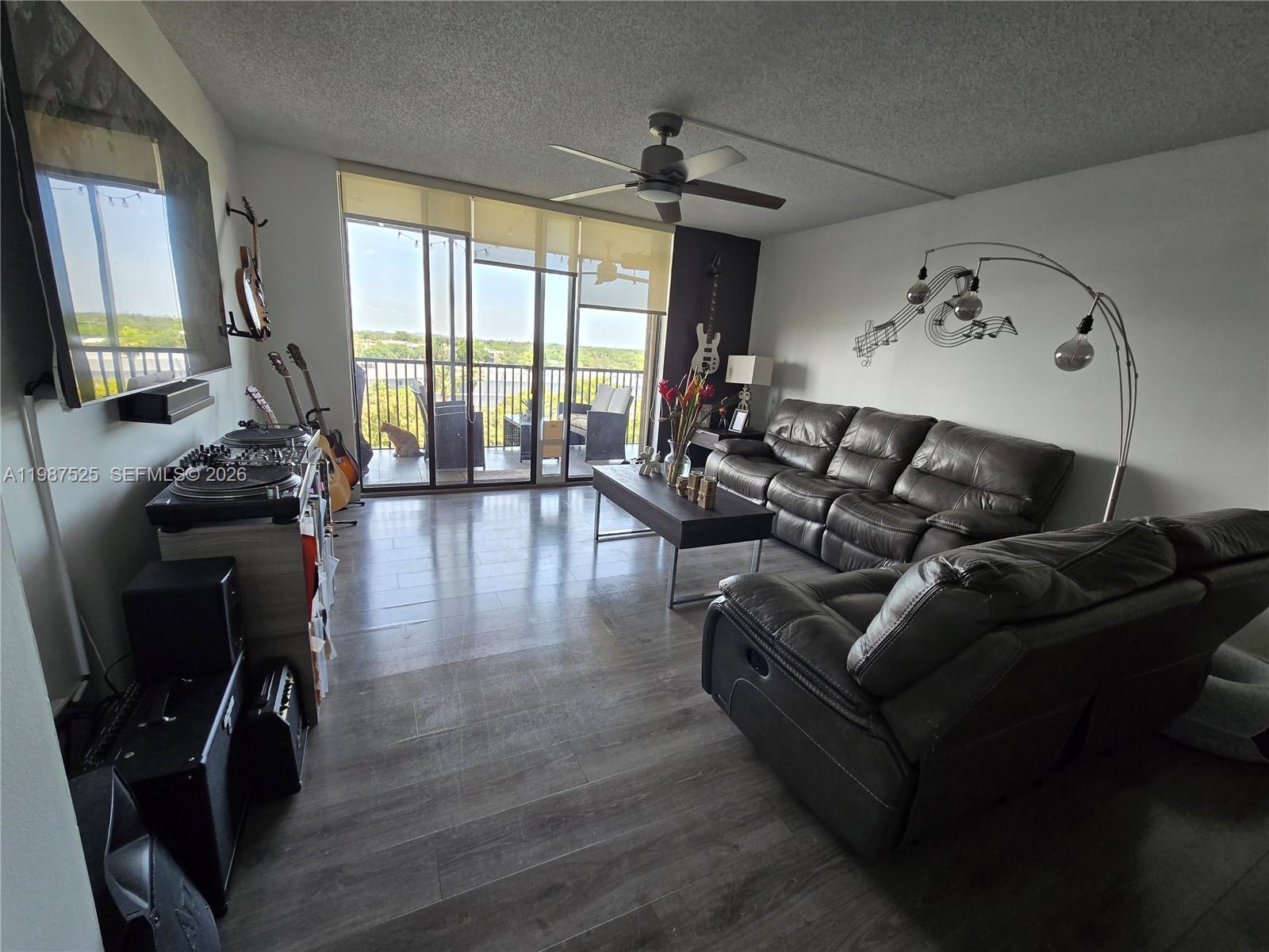 A living room features dark leather sofas, a ceiling fan, and a balcony with views — 900 NE 195th St # 709, Miami FL 33179, MIAMI, FL